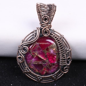 May include: A handcrafted pendant featuring a vibrant, polished, red and gold gemstone encased in intricate copper wire. The wirework forms a decorative frame and bail, creating a unique, artistic jewelry piece.