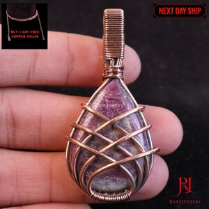 May include: A handcrafted pendant with a teardrop-shaped, purplish-pink stone, intricately wrapped in copper wire. The wirework forms a cage-like design around the stone. The pendant is suspended from a copper wire loop. The image also includes the text "25RareJewelry".