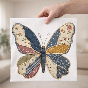 Op de afbeelding: Een vierkant wit stoffen paneel met een centraal vlinderontwerp bestaande uit diverse lapjes stof in tinten blauw, mosterdgeel, saliegroen en crème. De vlindervleugels zijn omlijnd met decoratieve stiksels.