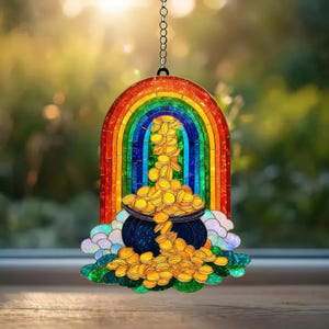 Könnte beinhalten: Ein Buntglas-Sonnenfänger mit einem leuchtenden Regenbogen, der sich über einen dunkelblauen Kessel wölbt, welcher mit Goldmünzen gefüllt ist. Das Design zeigt hellblaue und weiße Wolken an der Basis und hängt an einer silbernen Metallkette.