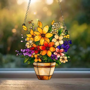May include: A stained glass suncatcher featuring a bouquet of vibrant yellow, orange, red, purple, and white flowers in a beige pot. The piece is suspended by a silver-toned metal chain, showcasing intricate glass segments and dark leaded lines.
