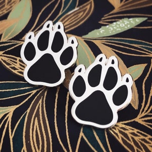 May include: Two black and white paw print pins. The pins are silver and have a shiny finish.