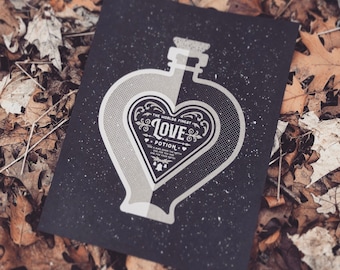 May include: A black and white illustration of a heart-shaped bottle with a label that reads "The World's Finest Love Potion". The bottle is on a black background with white speckles.