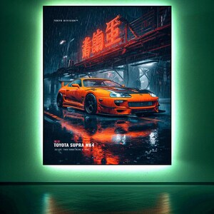 May include: A rectangular wall art print featuring an orange Toyota Supra MK4 parked on a wet city street at night. The scene includes red neon kanji signage, rain, and reflections. Text reads TOKYO DIVISION, TOKYO, TOYOTA SUPRA MK4, 2JZ-GTE.