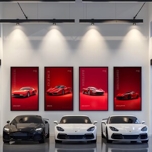 May include: Four framed vertical posters featuring red sports cars labeled Testarossa, Enzo, Daytona, and Competizione are displayed on a white wall above three luxury sports cars, one black and two white, parked on a polished gray floor.