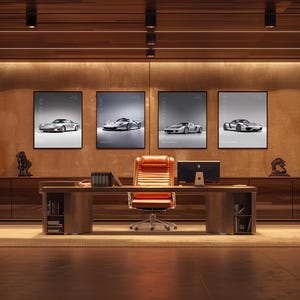 May include: A modern office space featuring a large wooden desk with an orange leather chair, a computer monitor, and four framed wall prints displaying silver sports cars. The room includes two orange armchairs and warm lighting.