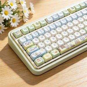 May include: A mechanical keyboard with a light green frame and rounded keys in pastel blue, white, and green. Several keys feature small, colorful illustrations of buildings, animals, and objects. The space bar displays a graphic of cartoon animals.