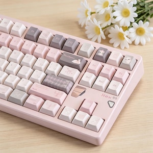 May include: A mechanical keyboard with a light pink frame and a mix of white, light pink, and grey keycaps. Several keys feature small illustrations of rabbits, bows, and carousel horses. The text Hex 90 is printed on the lower right corner.