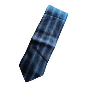 Peut inclure: Une cravate bleu marine avec un motif r&eacute;p&eacute;t&eacute; de petites fleurs rouges. La cravate pr&eacute;sente une texture g&eacute;om&eacute;trique subtile et est l&eacute;g&egrave;rement inclin&eacute;e, mettant en valeur sa longueur et son design.