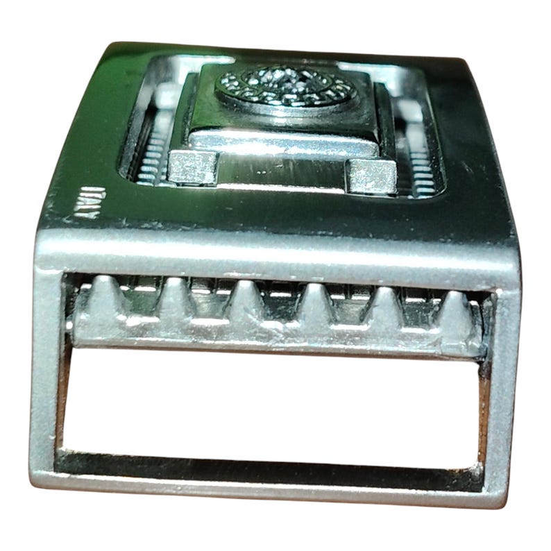 K&ouml;nnte beinhalten: Silberfarbene Metallschnalle mit rechteckiger Form. Die Schnalle hat ein zentrales dekoratives Element und das Wort "ITALY" ist sichtbar. Die Schnalle hat ein strukturiertes Design und einen Dornverschluss.