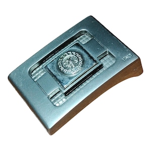 K&ouml;nnte beinhalten: Silberfarbene Metallschnalle mit rechteckiger Form. Die Mitte zeigt einen quadratischen Einsatz mit einem kreisf&ouml;rmigen Emblem. Das Wort "ITALY" ist sichtbar. Die Schnalle hat ein strukturiertes Design.