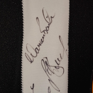 May include: Close-up of a black and white striped fabric with handwritten signatures in black ink. The signatures are on a white stripe, with a black background on either side.