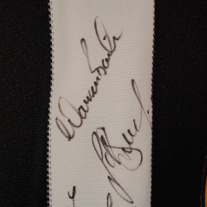 May include: Close-up of a black and white striped fabric with handwritten signatures in black ink. The signatures are on a white stripe, with a black background on either side.