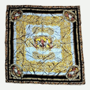 May include: A square silk scarf featuring a light blue center with a central gold ornate emblem depicting horses and figures. The border is black with gold filigree patterns and four circular corner medallions containing horse imagery.