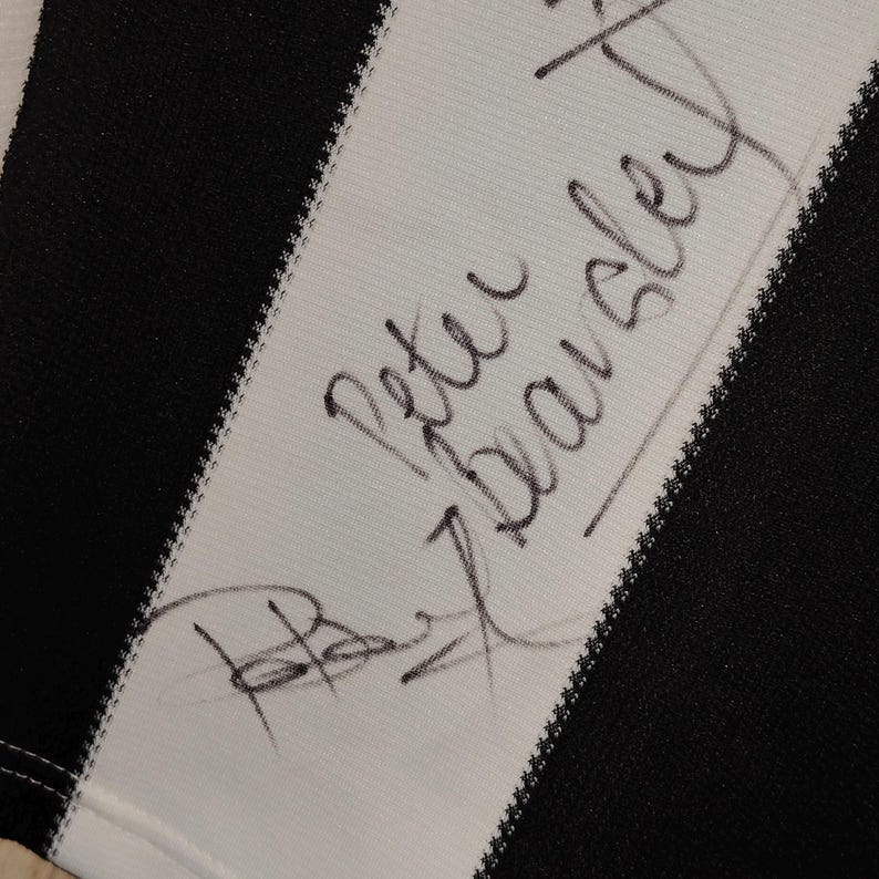 May include: Close-up of a black and white striped fabric with the handwritten signature "Peter Beardsley" in black ink. The signature is on a white stripe, with a black stripe visible.