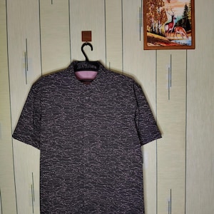 May include: A short-sleeved button-down shirt in a dark charcoal gray color featuring a fine, light-colored wavy line pattern across the fabric. The shirt has a classic collar, a front button placket, and a contrasting light pink inner lining.
