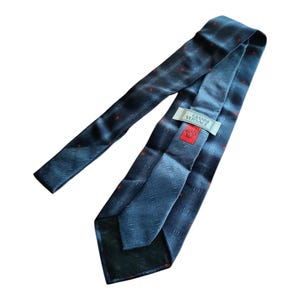 Peut inclure: Une cravate en soie bleu marine avec un motif g&eacute;om&eacute;trique subtil et de petits points rouges. La cravate porte une &eacute;tiquette avec le texte "GIANNI VERSACE" et un logo rouge. Un accessoire classique.
