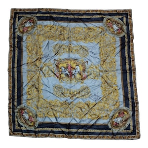 May include: A square silk scarf with a light blue center and a dark blue border. The scarf features ornate gold filigree designs and a central image of a chariot scene. The corners have oval portraits.