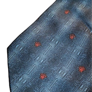 Peut inclure: Une cravate bleue avec un motif g&eacute;om&eacute;trique et de petits accents rouges. La cravate pr&eacute;sente un motif r&eacute;p&eacute;titif de carr&eacute;s et de lignes, avec des accents rouges espac&eacute;s sur le tissu. La cravate est faite d'un mat&eacute;riau brillant.