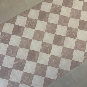 Könnte beinhalten: Eine Bodenfläche mit einem sich wiederholenden Schachbrettmuster aus quadratischen Fliesen in abwechselnden Farbtönen von hellem Beige und Altrosa. Jede Fliese weist eine natürliche, marmorartige Maserung auf, die ein klassisches Raster bildet.