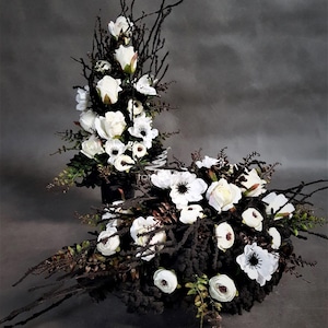 Könnte beinhalten: Ein Blumenarrangement mit weißen Rosen und weißen Anemonen mit dunkler Mitte, akzentuiert durch schwarze Zweige, dunkles strukturiertes Laub und farnartiges Grün. Die Komposition besteht aus einem hohen vertikalen Gesteck und einem runden.