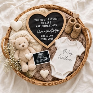 May include: A round wicker basket containing a heart-shaped letter board with the text THE BEST THINGS IN LIFE ARE SOMETIMES Unexpected ARRIVING JUNE 2026, a beige teddy bear, a white baby bodysuit labeled Baby William, booties, and an ultrasound.