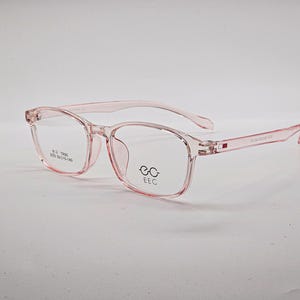 May include: A pair of transparent pink eyeglasses with a square frame. The glasses have a clear lens and a pink frame. The brand logo "EEC" is visible on the frame. The frame size is 52-16-140.