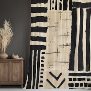 May include: A large, patterned curtain with a beige background and bold black geometric designs. The curtain features stripes, rectangles, and arrow-like shapes. The curtain is hanging in front of a dark gray wall.