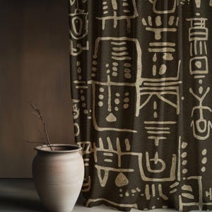 May include: Dark brown curtain with a cream geometric pattern. A beige ceramic vase with a dried branch is in front of the curtain. The curtain design features abstract shapes and lines.