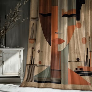 May include: A beige curtain with an abstract face design in shades of brown, orange, and black. The artwork features geometric shapes and lines, creating a modern, artistic aesthetic. The curtain is hanging in front of a white cabinet and a vase of flowers.