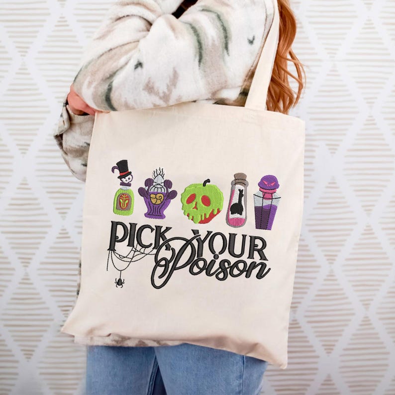 May include: Cream-colored tote bag featuring embroidered Halloween-themed designs of potion bottles and a green apple. The phrase "PICK YOUR POISON" is written in black script. A spider and web are also embroidered on the bag.