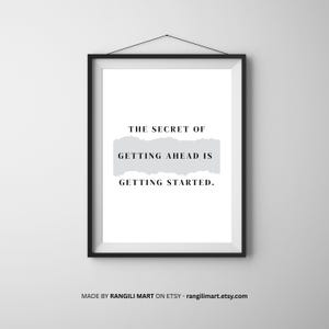 May include: A framed print with a black frame and a white background. The text "THE SECRET OF GETTING AHEAD IS GETTING STARTED" is displayed in black font. A light gray rectangle is behind the text. The print is hanging on a white wall.