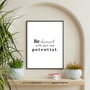 Könnte beinhalten: Gerahmter Druck mit dem Text "Be obsessed with your own potential" in schwarzer Schrift auf weißem Hintergrund. Der Druck wird auf einem Holzregal mit kleinen Topfpflanzen und Büchern ausgestellt.