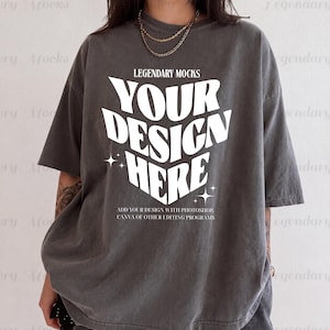 May include: A charcoal gray oversized t-shirt with the text "YOUR DESIGN HERE" in a bold, white, 3D-style font. The shirt also features the text "LEGENDARY MOCKS" and "ADD YOUR DESIGN WITH PHOTOSHOP, CANVA OF OTHER EDITING PROGRAMS".