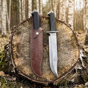 May include: Two survival knives with black handles and silver blades are displayed on a tree stump. One knife is in a brown leather sheath. The blades have a sharp edge and a wide profile, suitable for outdoor activities.