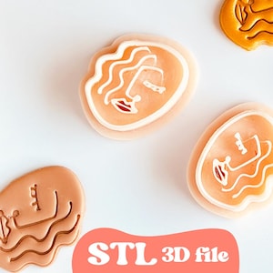 May include: An overhead shot displays several abstract face-shaped objects. Some are peach-colored with white and red details, while others are a darker brown. The objects are scattered on a white surface. The text "STL 3D file" is at the bottom.