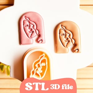 May include: Three face-shaped cookie cutters in shades of pink and peach, arranged on a white surface. The cutters feature a minimalist face design with flowing hair. The bottom cutter is inside a peach-colored frame. The text "STL 3D file" is at the bottom.