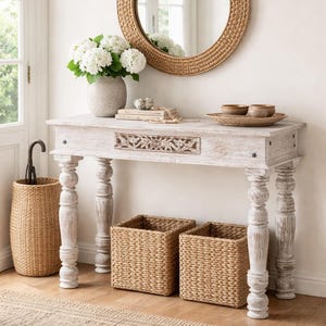 May include: A rustic entryway scene featuring a distressed white console table with carved drawer detail, a woven mirror, and matching baskets. A vase of white flowers and a woven umbrella stand complete the decor. A jute rug adds texture.