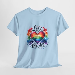 Może przedstawiać: Jasnoniebieski t-shirt z centralną grafiką serca w kolorach tęczy, otoczonego kolorowymi plamami akwareli. Napis "Love is for All" jest nadrukowany czarną czcionką przypominającą pismo odręczne nad i pod sercem na klatce piersiowej.