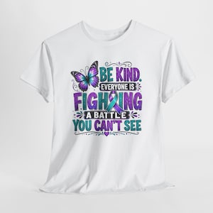 Könnte beinhalten: Ein weißes kurzärmeliges T-Shirt mit einem Grafikdruck eines violetten und blauen Schmetterlings, einer türkisfarbenen und violetten Schleife sowie dem Text: BE KIND. EVERYONE IS FIGHTING A BATTLE YOU CAN'T SEE. Das Design enthält Verzierungen.