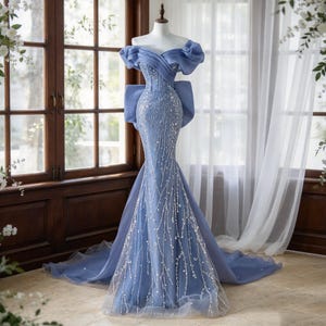 Könnte beinhalten: Ein bodenlanges, kornblumenblaues Kleid mit schulterfreiem Ausschnitt, voluminösen drapierten Ärmeln, einem figurbetonten Oberteil und einem ausgestellten Rock. Das Kleid ist mit aufwendigen silbernen Perlenstickereien und Pailletten verziert.
