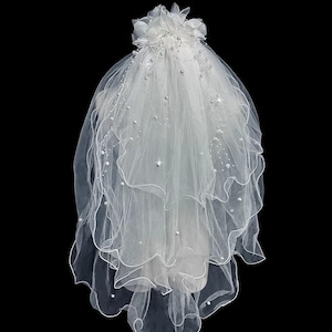 Puede incluir: Un velo de novia blanco con múltiples capas de tela transparente. El velo está adornado con pequeñas perlas y detalles brillantes. Un grupo de flores de tela blanca en la parte superior. Para una boda.