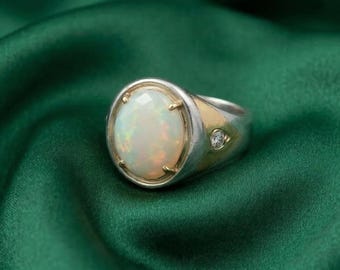 May include: A silver and gold ring with a large, oval opal gemstone. The opal has a milky white color with flashes of color. A small diamond is set on the side of the ring.