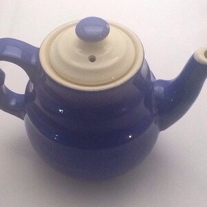 May include: A blue ceramic teapot with a white lid and a small spout. The teapot has a rounded body and a handle.
