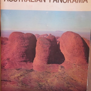 Puede incluir: Una portada de revista vintage que presenta una vista panorámica de formaciones rocosas rojas en el interior de Australia. La portada dice "AUSTRALIAN PANORAMA".