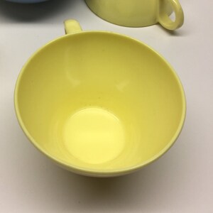 May include: A yellow ceramic teacup with a handle. The cup is empty and the inside is visible.
