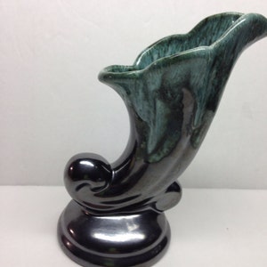May include: A green and black ceramic vase with a unique, curved design. The vase has a glossy finish and a wide opening.