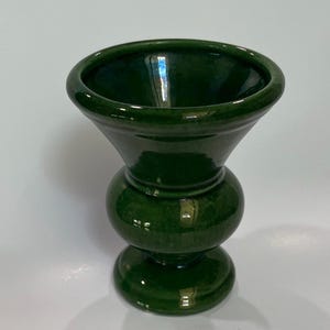 May include: A glossy, dark green ceramic vase with a bulbous body and a flared top. The vase has a rounded base and a smooth, reflective surface. The design is a modern take on a classic shape, suitable for displaying flowers or as a decorative accent.