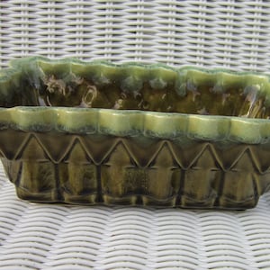 以下が含まれることがあります： 緑色の釉薬がかけられたセラミック製のプランターで、縁が波打っていて、幾何学模様が施されています。プランターは角が丸みを帯びた長方形の形をしています。