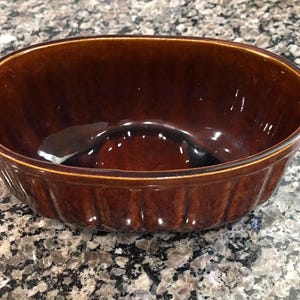 May include: A brown ceramic oval baking dish with a fluted rim. The dish is empty and ready to be used for baking.